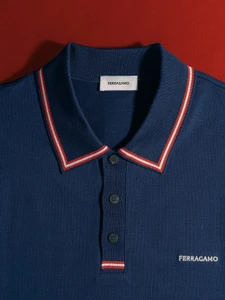 Close-up of a navy blue Ferragamo polo shirt with red and white striped collar detail against a deep red background.