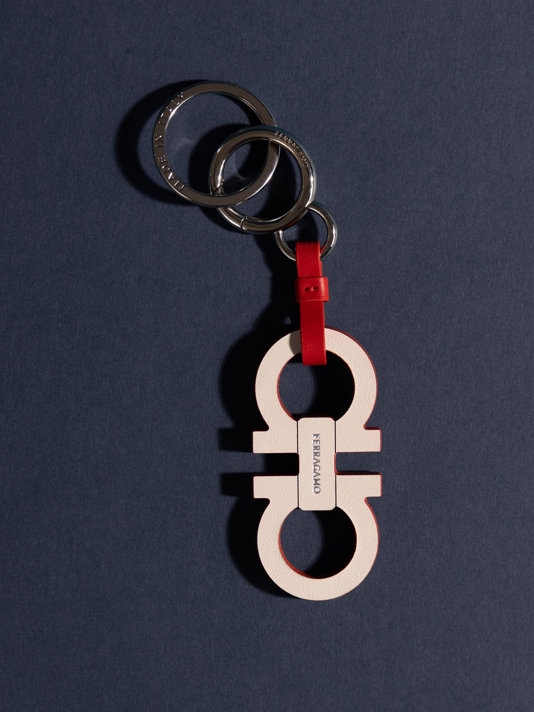 Ferragamo leather Gancini keychain with red detailing and silver split rings resting on a dark slate background.