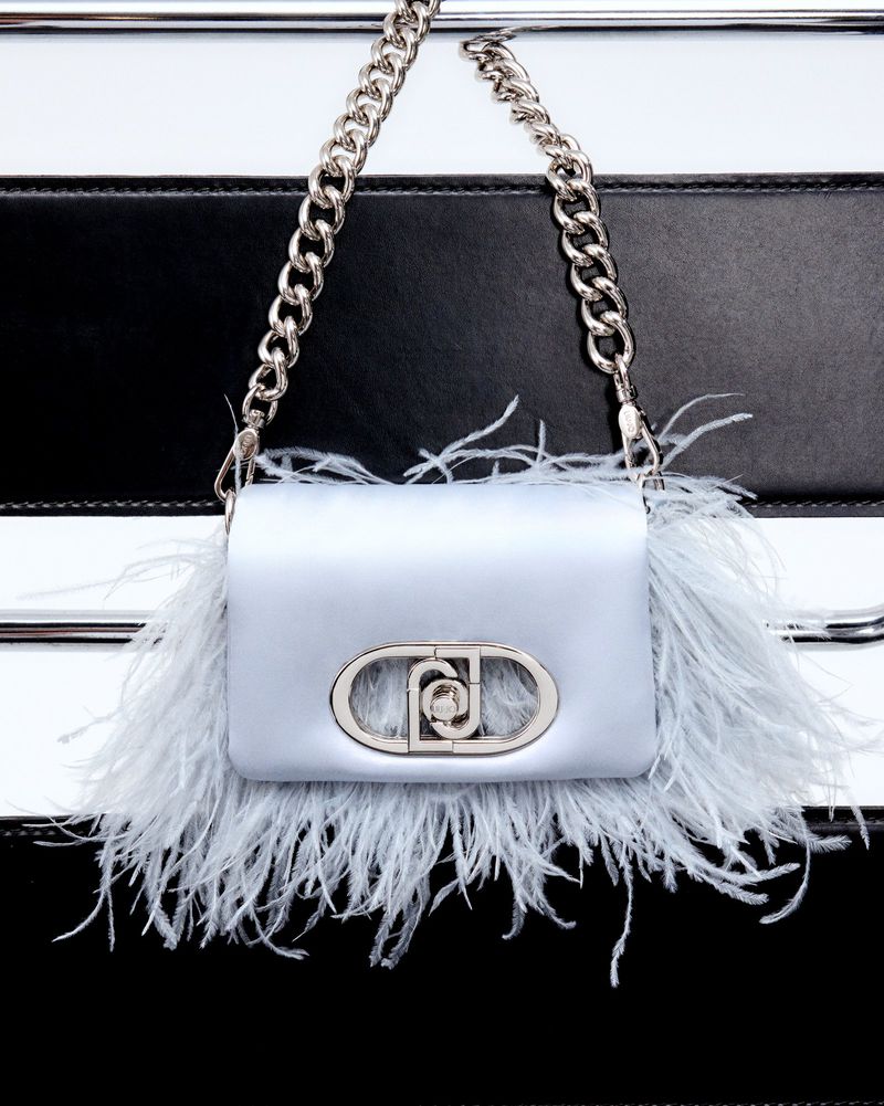 Close-up of a light-blue handbag with ostrich feathers and a silver chain strap against a black and white striped background.