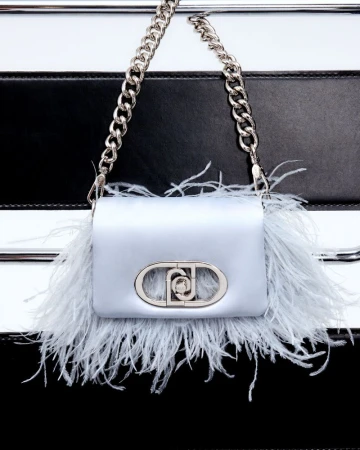 Close-up of a light-blue handbag with ostrich feathers and a silver chain strap against a black and white striped background.