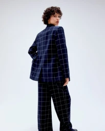 Model with curly dark hair wearing a navy blue checkered pantsuit against a plain light background