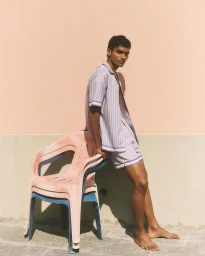 Model Deepak Gupta leaning on stacked plastic chairs wearing a matching patterned shirt and shorts against a warm wall.