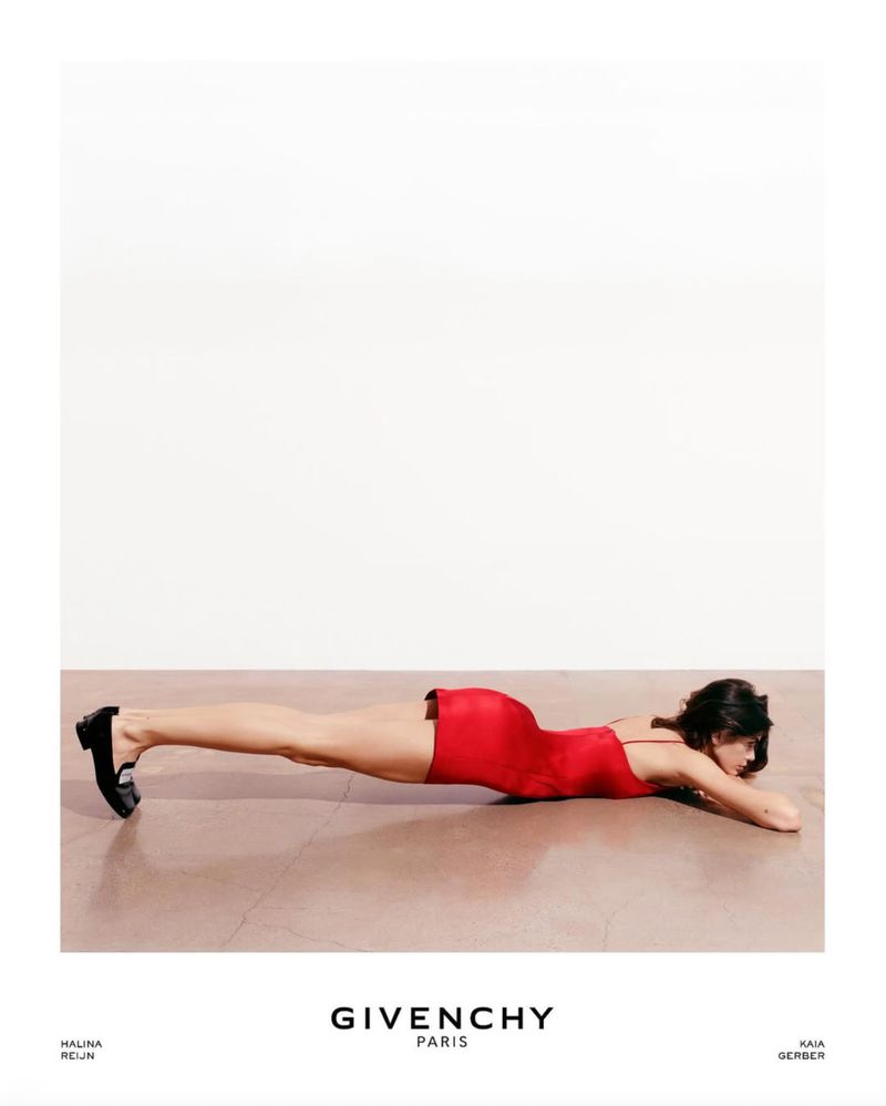 Woman in a red dress lying on the floor with her arms outstretched in a studio setting for a fashion advertisement.