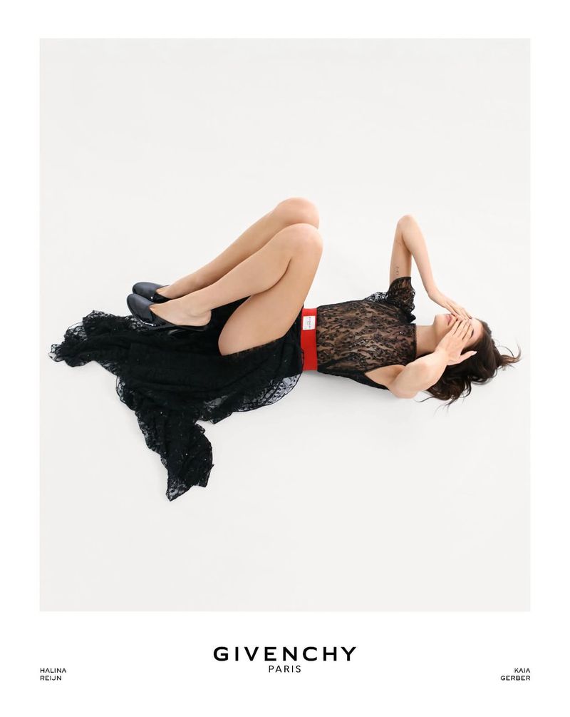 Fashion shoot features a model in a black lace dress with a red belt, lying on a white background, covering her face.