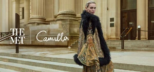 Woman wearing ornate patterned coat with black fur trim on classical stone building steps for The Met x CAMILLA campaign.