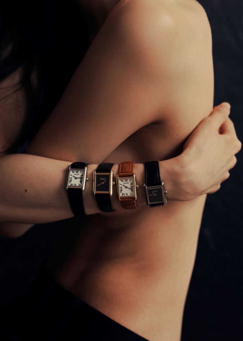 Four rectangular leather-strap wristwatches worn in a row along a bare forearm hugging a torso against a dark background.