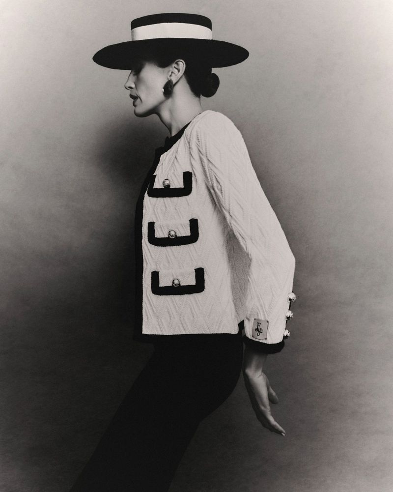 Profile portrait of a model wearing a wide-brimmed flat hat and a textured cardigan with contrasting trim against a neutral studio backdrop