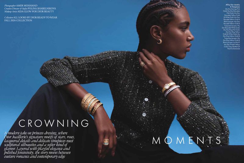 Black woman with braided hair wearing a dark sparkly cardigan and gold jewelry against a vibrant blue studio backdrop.