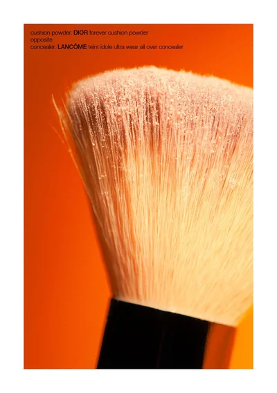 Close-up of a cosmetic makeup brush dusted with fine loose powder against a vibrant warm orange background.