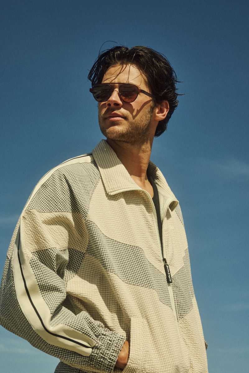 Matt Cornett wearing sunglasses and a textured cream zip jacket outdoors against a clear blue sky.