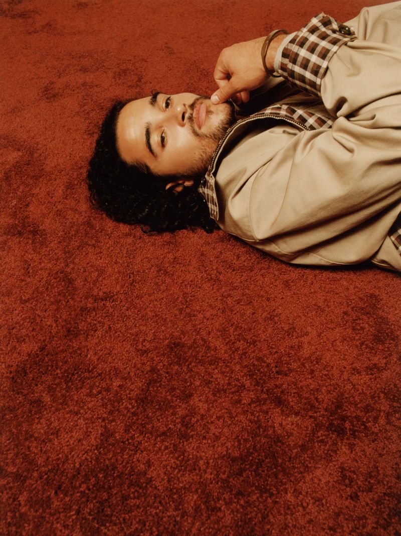 Actor Jalen Thomas Brooks lying on a textured red carpet wearing a tan jacket with plaid cuffs.