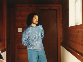Actor Jalen Thomas Brooks wearing a blue star-patterned knit sweater and blue trousers in a wood-paneled room.