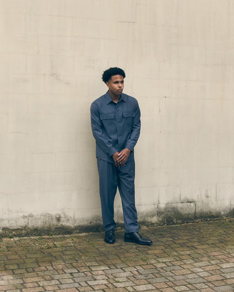 Weston McKennie standing outdoors in a slate blue button-up shirt and matching trousers against a pale weathered wall.