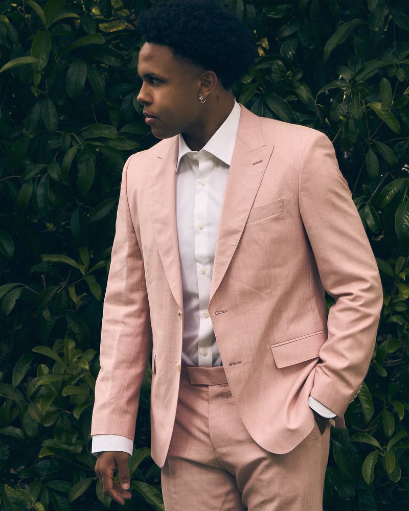 Weston McKennie in a tailored pink suit and white dress shirt posing in profile against green foliage
