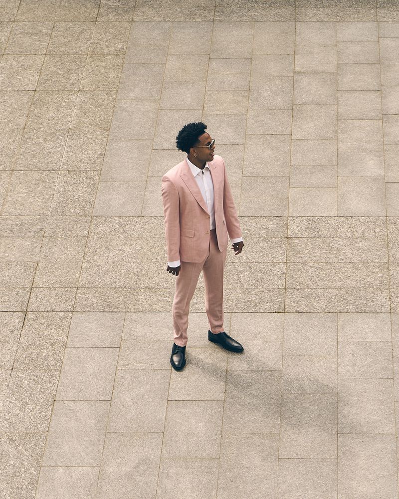Weston McKennie wearing a pale pink suit, sunglasses, and black dress shoes, standing outdoors on stone pavement.