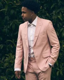 Weston McKennie in a tailored pink suit and white dress shirt posing in profile against green foliage