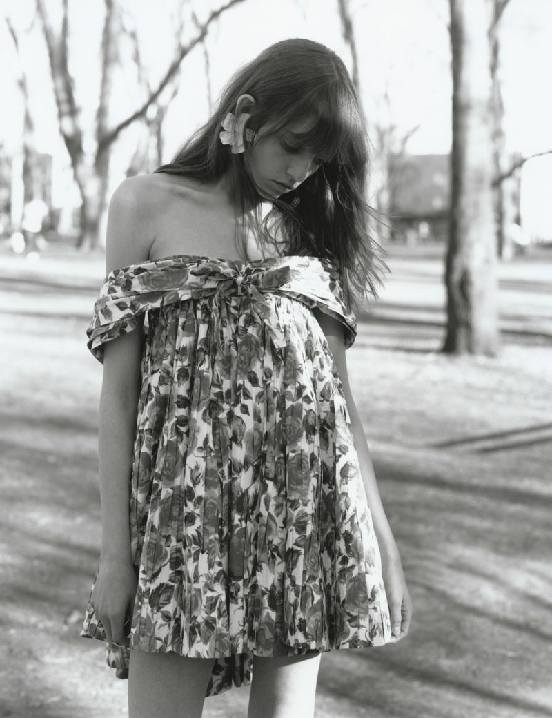 A woman looking down outdoors wearing an off-the-shoulder floral mini dress and a sculpted ear cuff in black and white.
