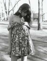 A woman looking down outdoors wearing an off-the-shoulder floral mini dress and a sculpted ear cuff in black and white.