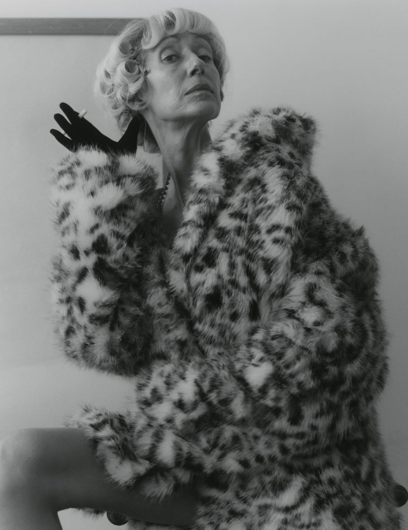 Monochrome portrait of a mature woman in a spotted faux-fur coat wearing black gloves and holding a cigarette.