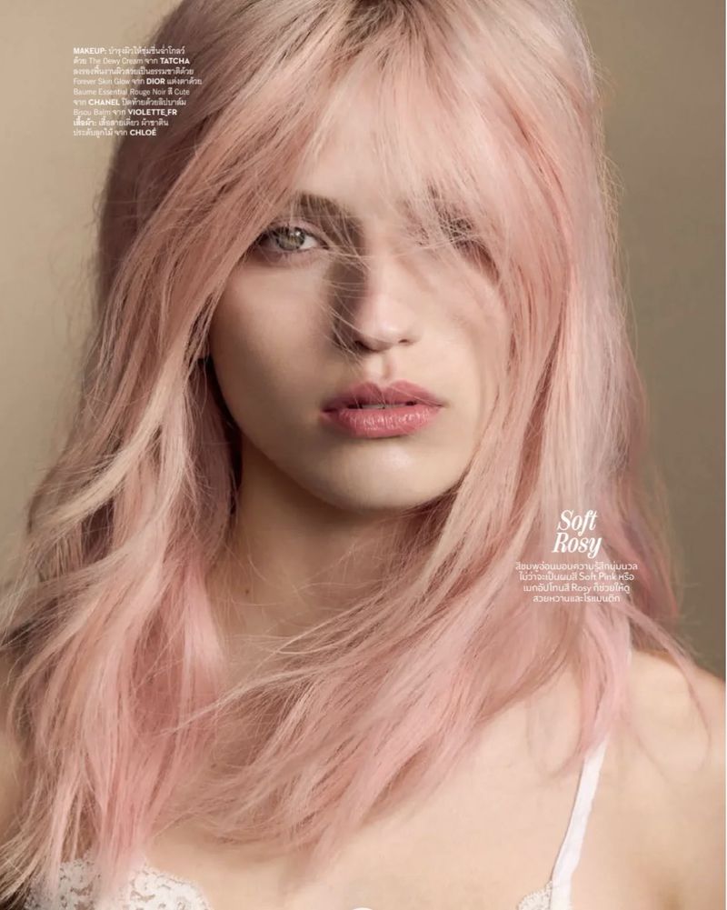 Close-up beauty portrait of a woman with pastel pink hair and fringe looking at the camera in a white lace top.