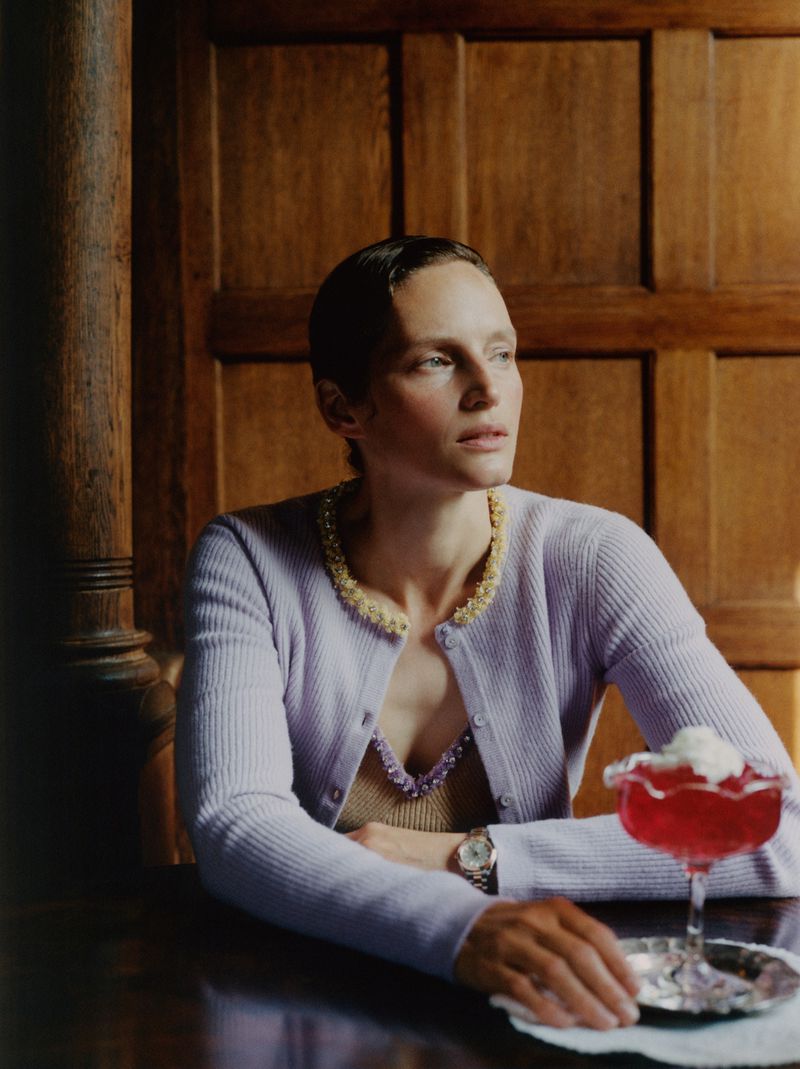Portrait of a woman in a lilac cardigan sitting at a table with a dessert, showcasing fashion, indoor setting, and natural lighting.