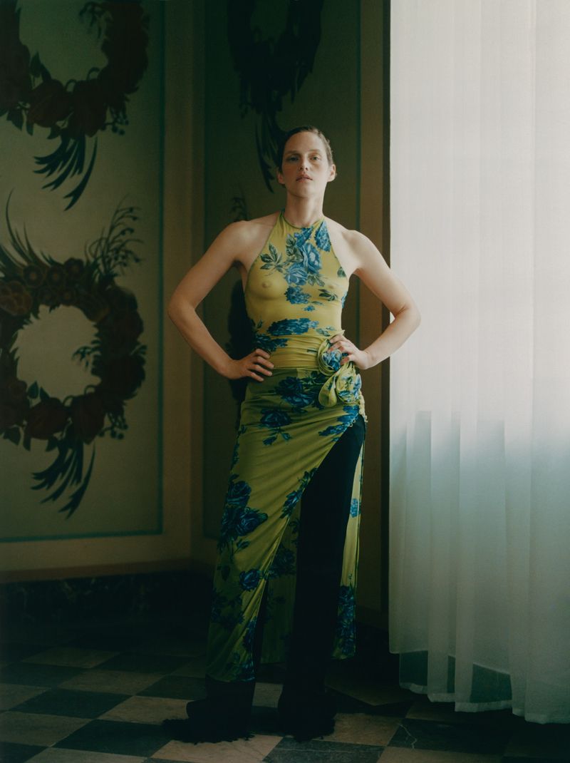 Adult female in floral print halter top and matching skirt posing indoors with hands on hips in front of decorative wall art.