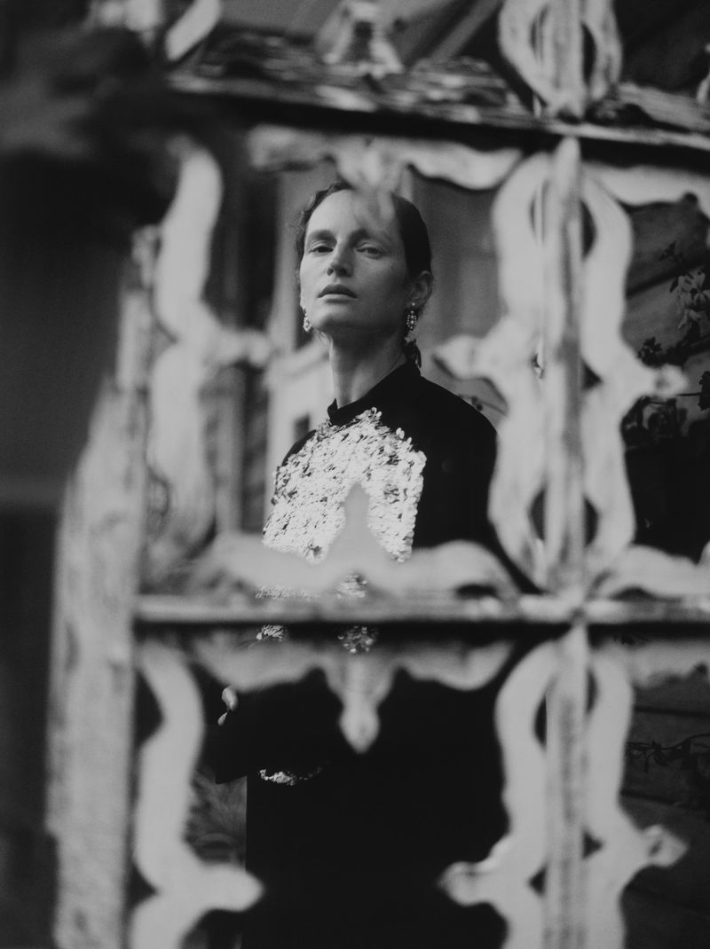 Black and white portrait of model Vivien Solari framed through an ornate decorative lattice wearing an embellished black dress.