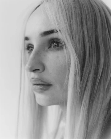Black and white close-up portrait of Kim Petras with long straight hair looking slightly aside against a light backdrop.