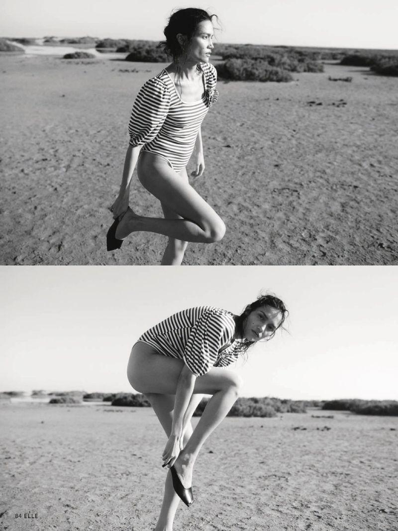 Black and white diptych of Charlotte Carey posing in a striped puff-sleeve bodysuit while putting on flat shoes on a sandy landscape.