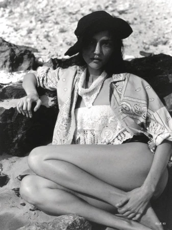 Model wearing a patterned shirt and hat seated among rocky terrain for Elle Italia editorial