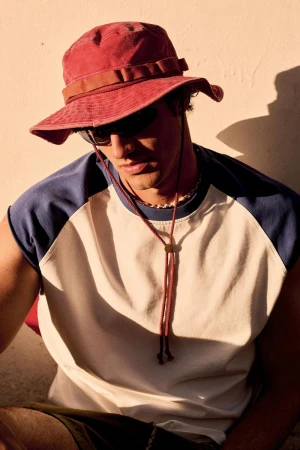 Model Francesco Ruggiero wearing a red boonie hat, dark sunglasses, and a cream and blue raglan shirt for Zara Man.
