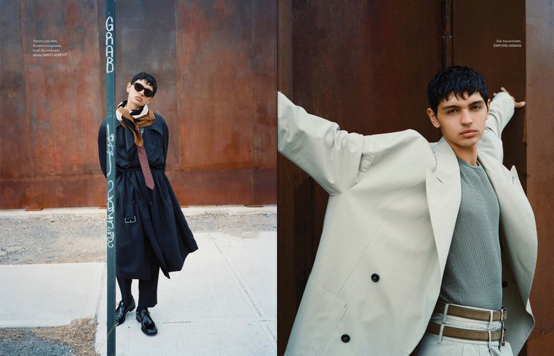 Editorial fashion shot: a young adult poses in a black trench coat next to a pole with graffiti, another poses in a tan coat against metal.