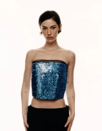 Gracie Abrams posing in a strapless blue sequined tube top and black skirt against a white studio background.