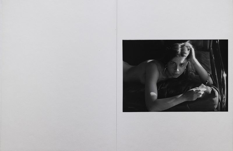 Monochrome editorial photo of a woman reclining with her head resting on her hand, set against an open white page layout.