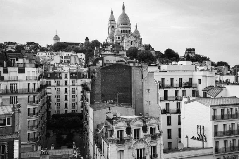 Black and white cityscape featuring the Sacré-Cœur Basilica in Paris, viewed from a high angle showcasing rooftops and architectural details.