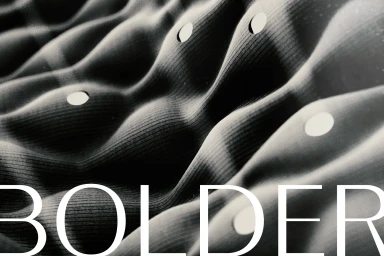 Monochrome close-up of undulating ribbed fabric with circular cutouts behind white typography reading BOLDER.