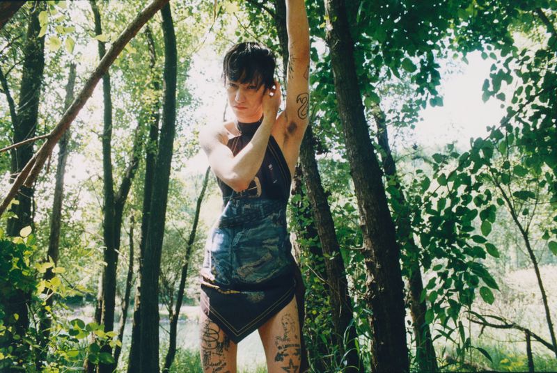 Model Valentino Pavesi poses among trees wearing a printed halter mini dress with arm raised for Magliano Lele SS26.
