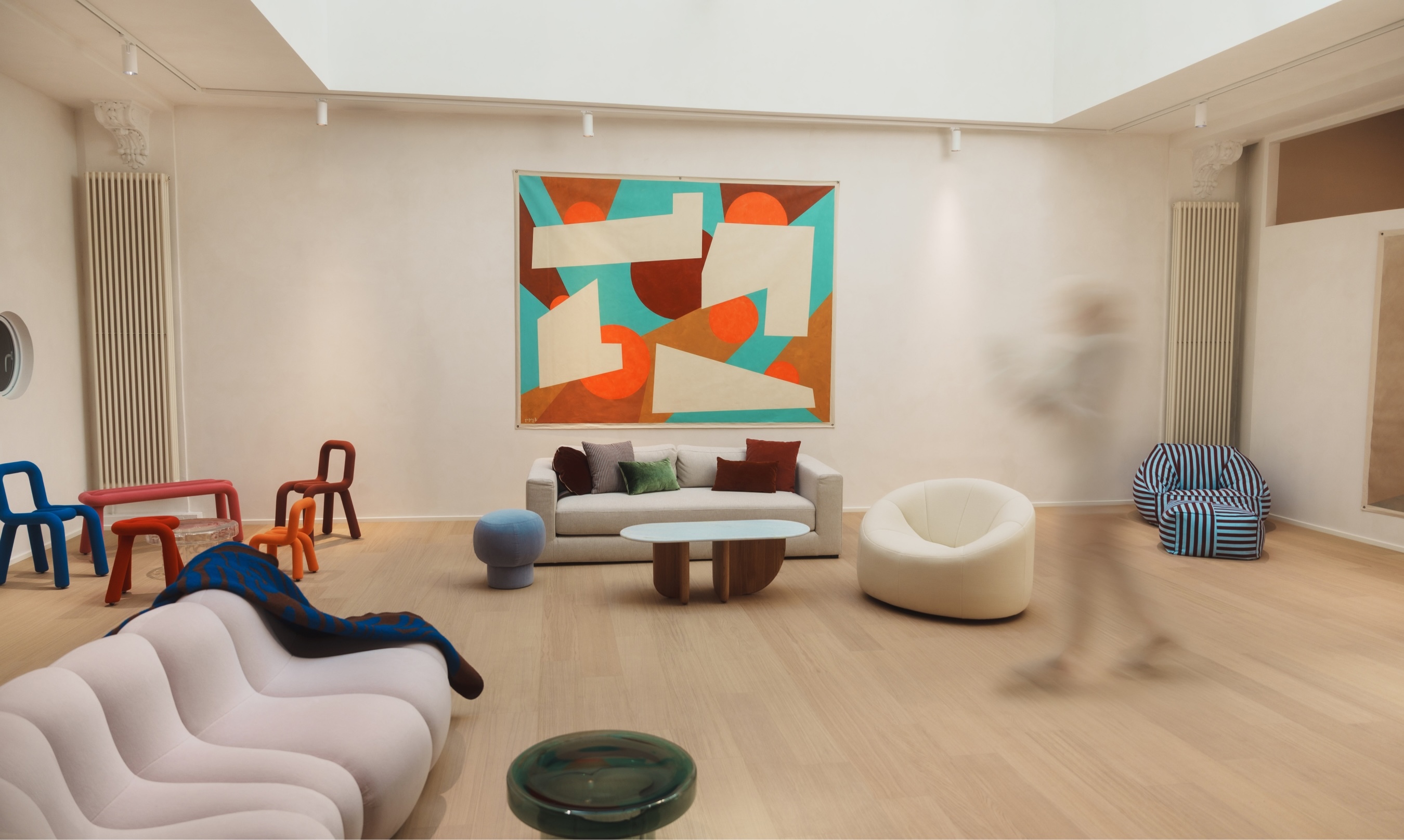 Modern interior showroom featuring sculptural furniture, colourful accent chairs, geometric wall art, and a motion-blurred person.