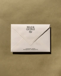 White paper envelope featuring Belle & George printed branding and monogram, placed on a smooth olive paper background.