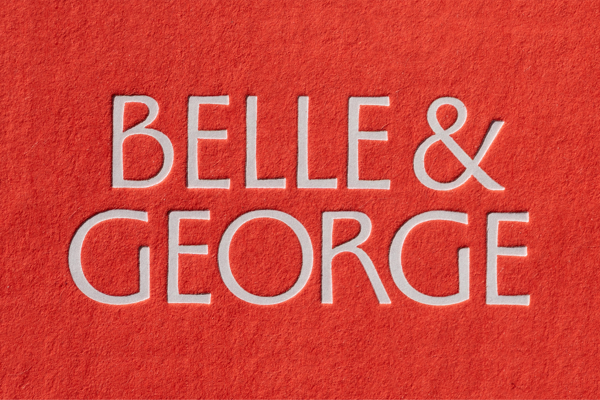White serif typography reading BELLE & GEORGE centered on bright red fibrous textured paper stock.