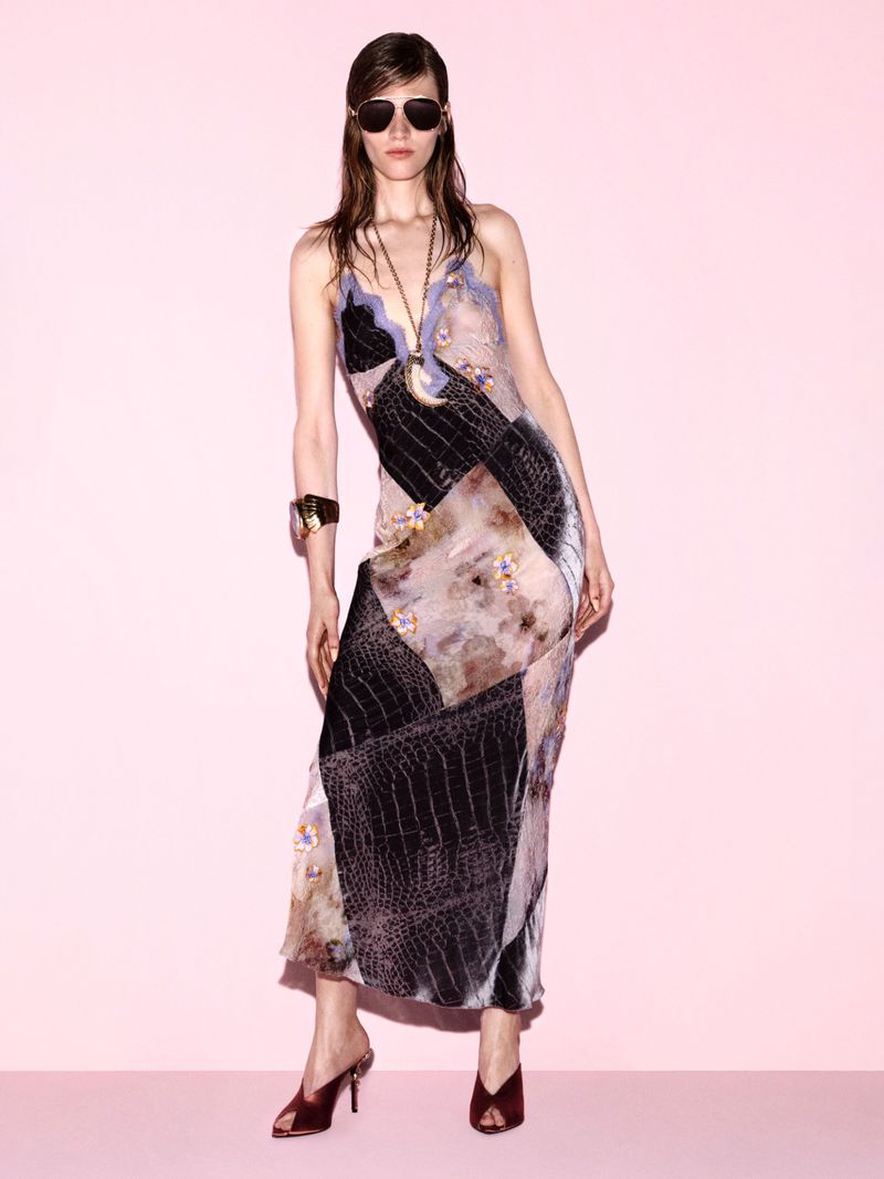 Model Leilani Mellor poses in a patchwork print slip dress, aviator sunglasses, and heeled mules against a light pink studio background.