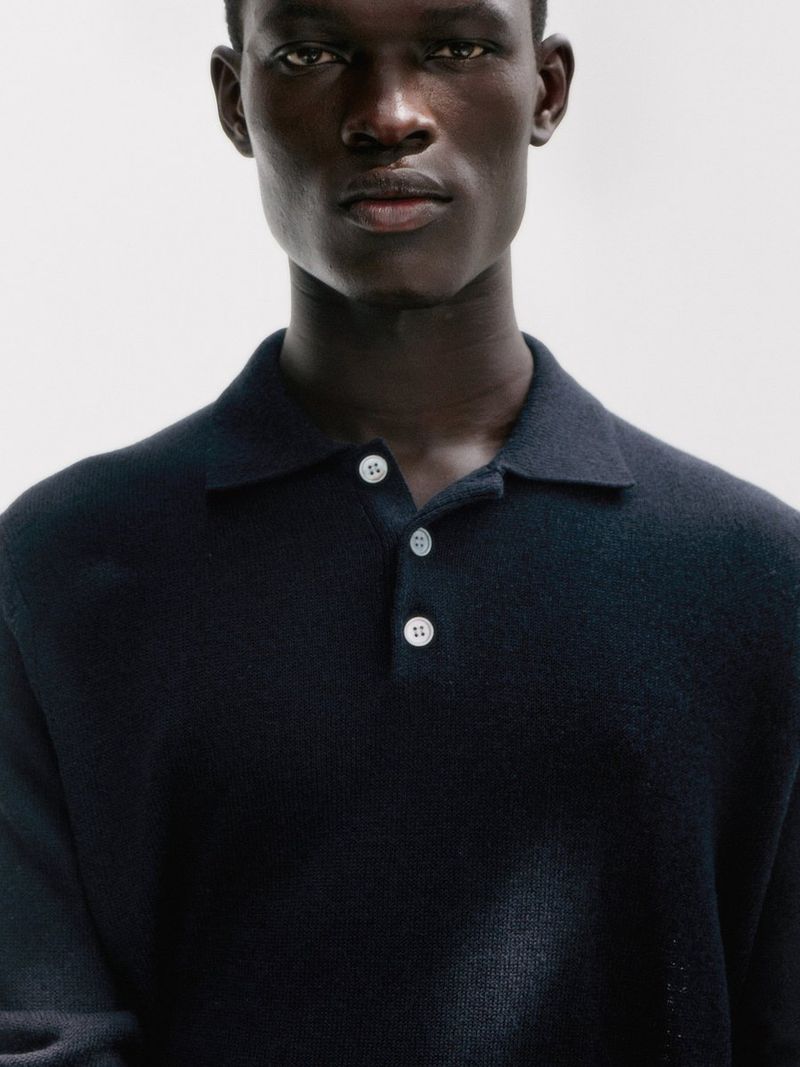 Model Gabriel Nhial wearing a dark navy knit polo sweater against a clean neutral studio backdrop for Arket.
