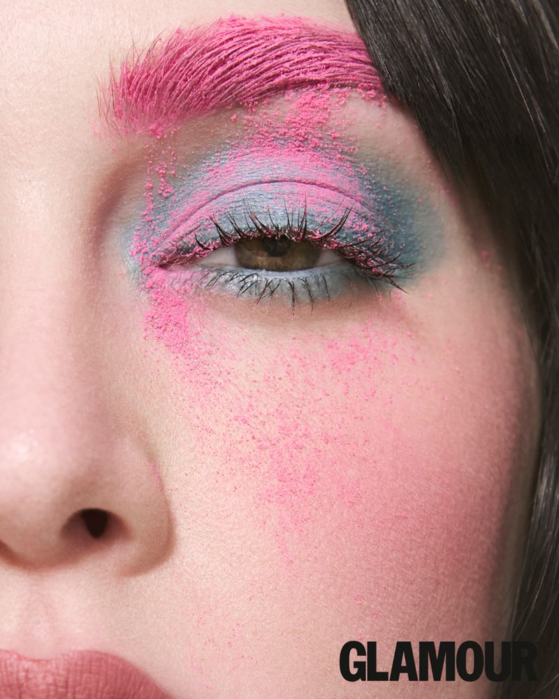 Close-up beauty portrait showing bright pink powder on eyebrow and cheek with blue eyeshadow and defined lashes.