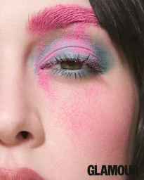 Close-up beauty portrait showing bright pink powder on eyebrow and cheek with blue eyeshadow and defined lashes.