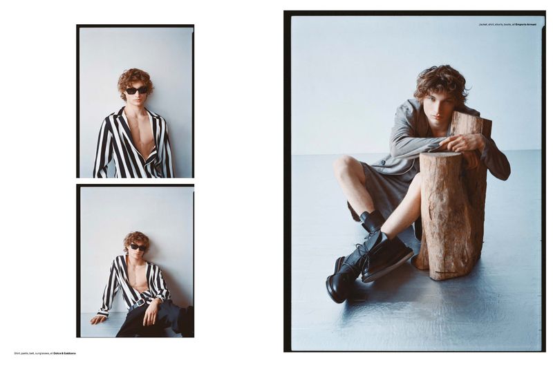 Editorial fashion shot featuring a young adult male in casual-chic attire posing in a photo studio with a log prop, set against a neutral backdrop.