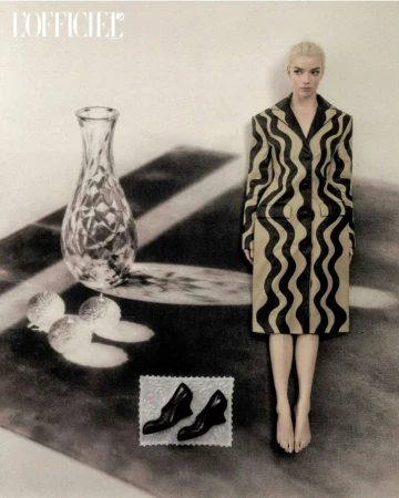 Anya Taylor-Joy wearing a patterned coat standing next to a vase on a table in an editorial photograph for L'Officiel Italia.