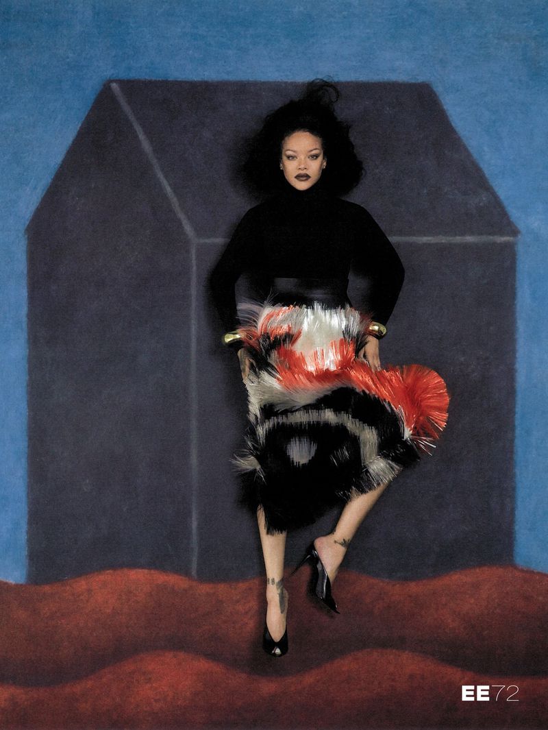 Rihanna wearing a black turtleneck and textured red and white fringe skirt against an illustrated dark house backdrop.