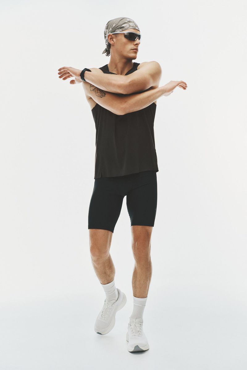 Model Finley Prentice stretches his arms wearing a black tank top, cycling shorts, sunglasses, and bandana against a white backdrop.