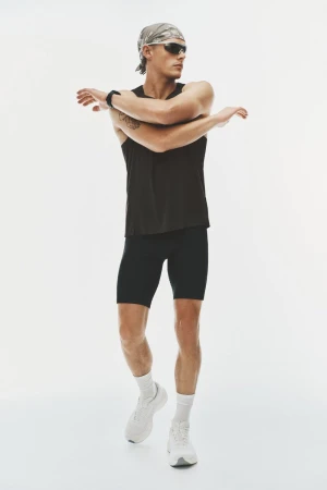 Model Finley Prentice stretches his arms wearing a black tank top, cycling shorts, sunglasses, and bandana against a white backdrop.