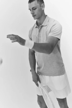 Black and white portrait of male tennis player Finley Prentice holding a racket in polo shirt against white background.